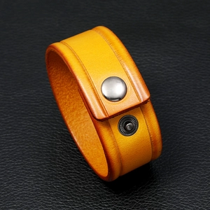Close-up of yellow leather bracelet with metal snap button on black textured background