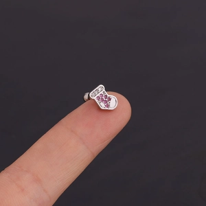 Vue macro d'une mini boucle d'oreille chaussette de Noël en argent avec zircons rouges sur un doigt
