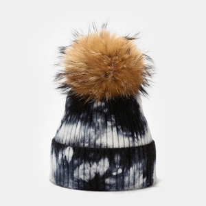 Close-up of black and white tie-dye knit hat with a fluffy brown pom-pom texture