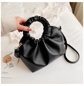 Detail of black pleated handbag featuring ruffled handle and shiny faux leather texture