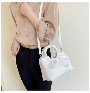 White ruched cloud handbag featuring woven handle and long shoulder strap on model