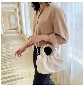 Detail of cream pleated cloud bag showing large ruffled handle and metal base feet