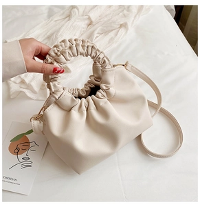 Detail of cream-white ruched leather handbag with circular handle and slender strap