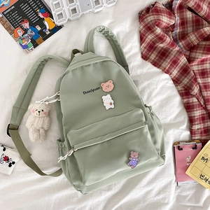 Close-up of pastel green nylon backpack with cute cartoon badges and small bear charm