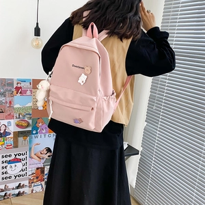Detailed close-up of a pink canvas school backpack featuring cute bear badges and a plush toy
