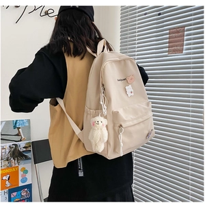 Detail of a beige nylon backpack with cute plush bear pendant and cartoon badges