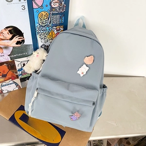 Detail of blue-grey nylon backpack featuring cute bear badges and a plush pendant accessory