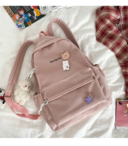 Detail of pink nylon backpack featuring cute bear badges and white plush charm on bed