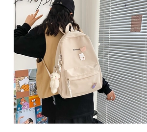 Detail of beige student backpack with cute plush charms and Duoqiyuan lettering