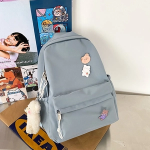 Detail of light blue nylon backpack with cute bear badges and white plush charm on desk
