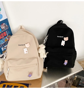 Detail of beige and black canvas backpacks with cute bear pins and embroidered lettering