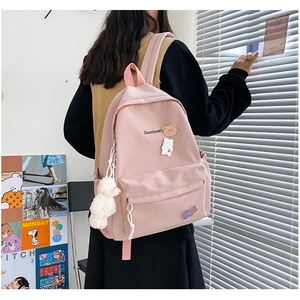 Detailed close-up of a pink canvas backpack with cute cartoon bear badges and a plush pendant