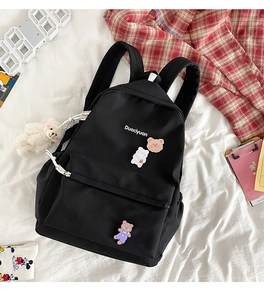 Flat lay of a cute black nylon backpack with Duociyuan text on a white bedsheet