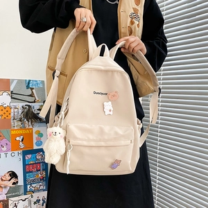 Detail of beige canvas backpack featuring cute cartoon pins and a plush white pendant