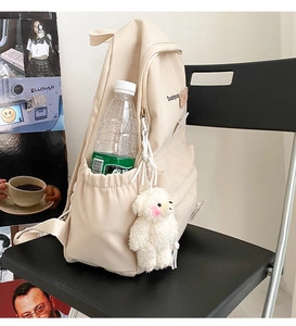 Detail of beige canvas backpack featuring side pockets and a cute white plush bear pendant