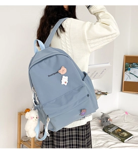 Detail of blue canvas backpack featuring cute plush bear charms and pins for students