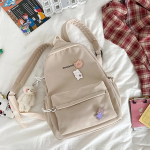 Detail of beige nylon backpack with cute bear pins and plush charm on white bedding
