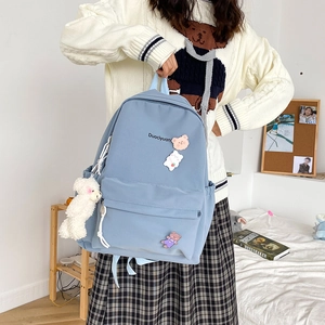 Detail of blue school backpack featuring cute bear badges and white plush pendant accessory