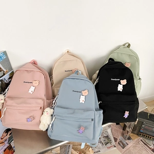 Close-up of minimalist school backpacks with cute bear patches and plush charms in five colors