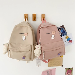 Detail view of cute school backpacks in beige and pink with plush bear charms and pockets