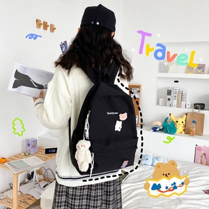 Detailed back view of a black canvas backpack featuring cute cartoon patches and a plush bear