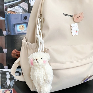 Detail of beige nylon backpack featuring cute plush bear charm and side pocket texture