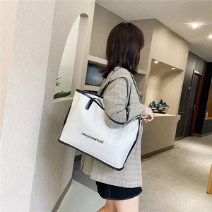 White minimalist tote bag with black contrast trim and thin shoulder straps worn by a model