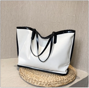 Detail shot of white canvas tote bag with black leather trim on a woven straw mat