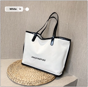 Close-up of a white canvas tote bag with black trim and JINGPINPIJU logo on straw mat