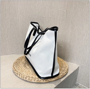 Detail of white canvas tote bag with black trim on a woven mat against a textured wall