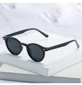 Detailed close-up of retro black round sunglasses with metal studs on white marble background
