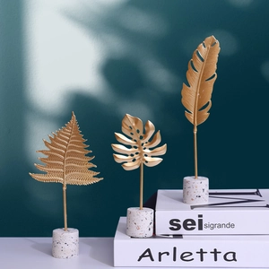 Gold monstera and fern metal leaf ornaments with white stone bases on books