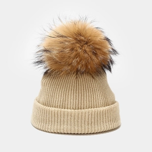Close-up of beige ribbed knit beanie with a fluffy brown faux fur pom pom detail