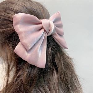 Close-up of pink organza bow hair clip with glossy pearl satin texture on hair