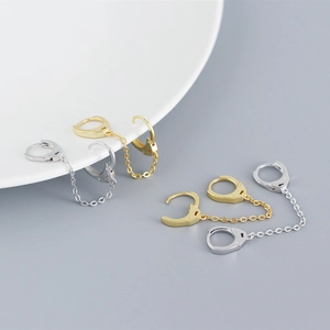 Detailed view of silver and gold handcuff-shaped chain earrings on ceramic plate