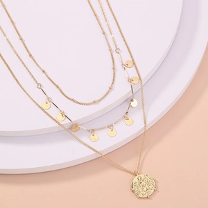 Detailed view of triple-layered golden necklace with coin pendant and disc accents