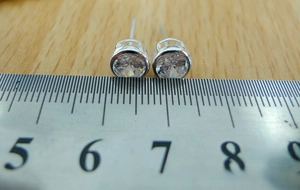 Detail view of 925 sterling silver stud earrings with 7mm clear zircon next to a scale