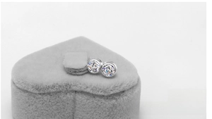 Detail of round bezel-set 925 silver stud earrings presented in heart jewelry box