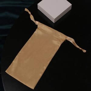 Golden satin drawstring pouch with silk ribbon and white gift box on dark background
