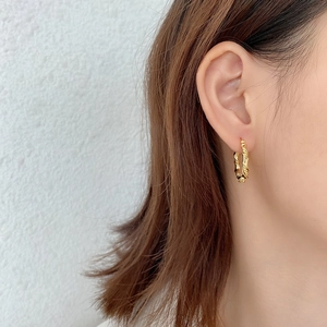 Close-up of golden twisted rope hoop earrings worn by a model for a stylish look