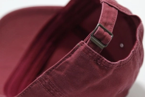 Detailed close-up of burgundy cotton canvas baseball cap with adjustable metal buckle strap