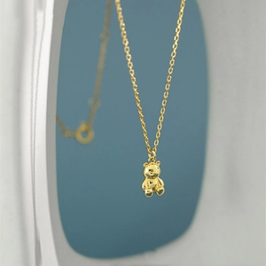 Close-up of a polished golden 3D bear pendant on a delicate cross chain necklace