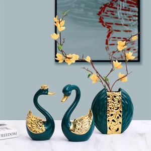 Modern emerald and gold ceramic swan statues with matching floral vase on marble surface