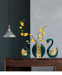 Detail of dark green ceramic swan figurines with gold trim and hollow decorative vase