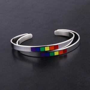 Detail of two rainbow enamel C-shape stainless steel bracelets on black stone
