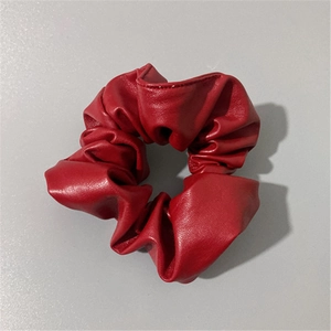 Macro detail of red faux leather scrunchie showing glossy pleated texture and premium stitching