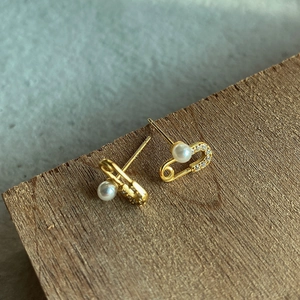 Detail of safety pin gold earrings with white pearls and zircons on a rustic wood surface