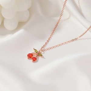 Close-up of a rose gold cherry necklace with red and green zircon crystals on white silk