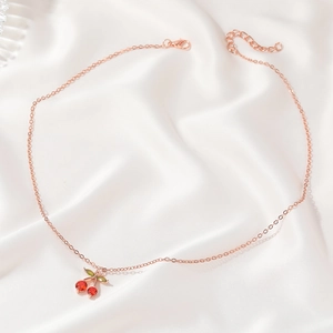Detail of rose gold cherry necklace with red and green zircons on white silk background