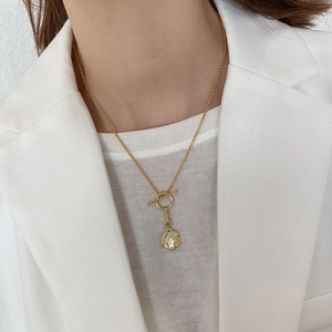Detail of gold coin pendant with OT buckle on white minimalist outfit background